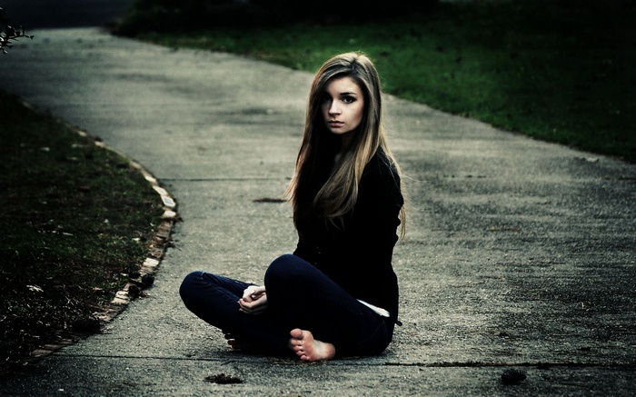 Woman with long hair sitting barefoot on a path