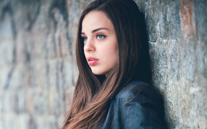 Young woman with blue eyes leaning against a stone wall