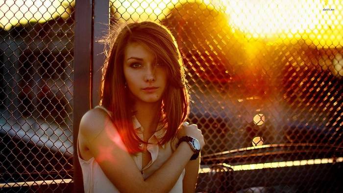 Young woman in front of a chain-link fence at sunset