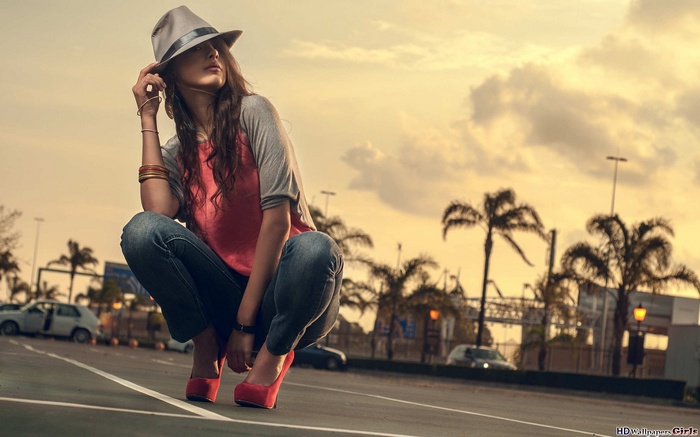 Woman in hat and jeans crouching outdoors