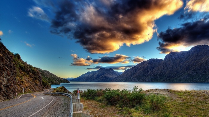 Road along a lake with mountains and dramatic clouds