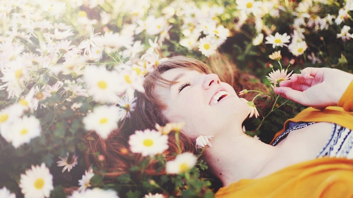 Woman laughing lying in a field of daisies