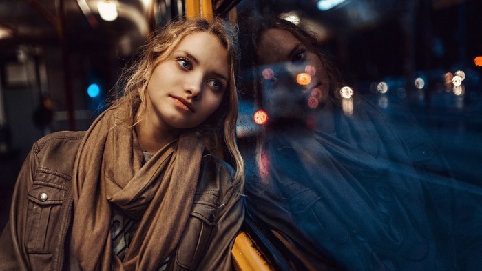 Woman with blonde hair and blue eyes reflected in a bus window