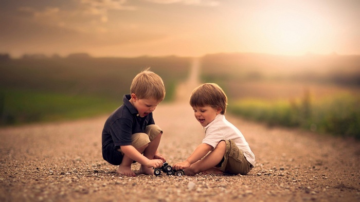 Two young boys playing with a toy car on a dirt road in Nebraska