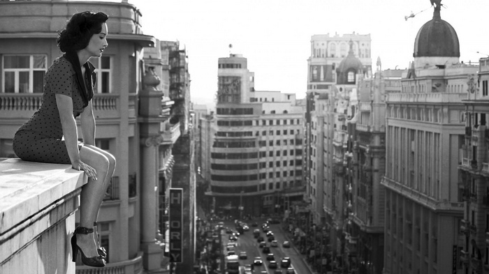 Woman in polka dot dress sitting on a rooftop overlooking a city street