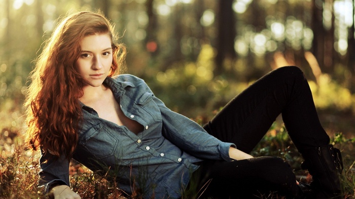 Woman with red hair lying in a forest
