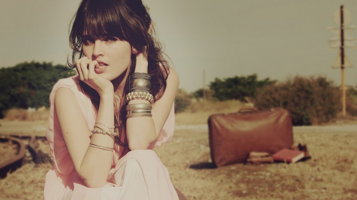 Woman with bracelets sitting outdoors with a suitcase