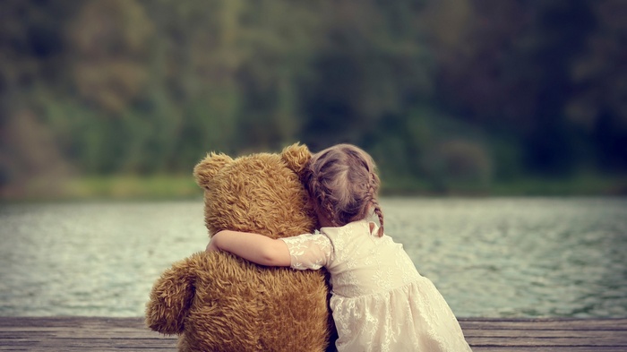 A girl hugs a teddy bear by a lake