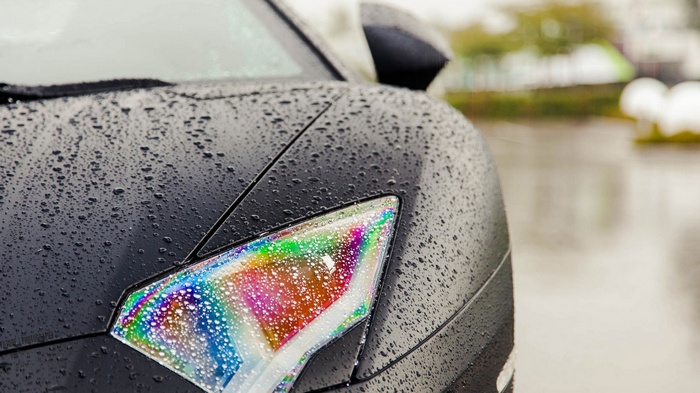 Black Lamborghini with rainbow headlights in the rain