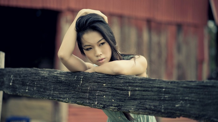 Asian woman leaning on a wooden fence