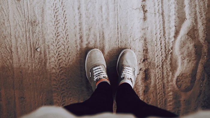 Person wearing Vans shoes on sandy ground with footprints