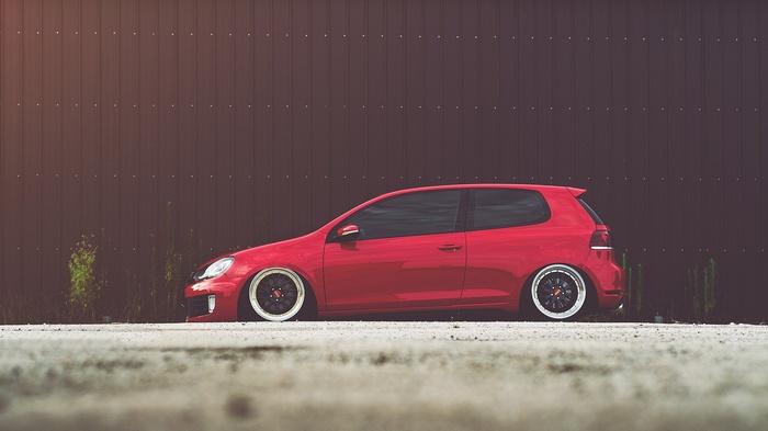 Red Volkswagen Golf VI parked against a dark wall