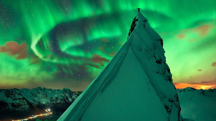 Man on mountain peak under Aurora Borealis in Norway