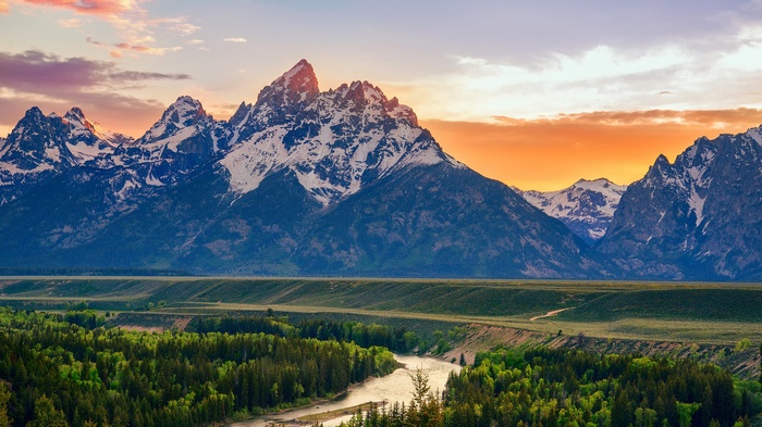 Snowy mountains at sunset over a forest and river