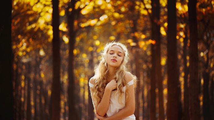 Woman with curly blonde hair in a forest during fall