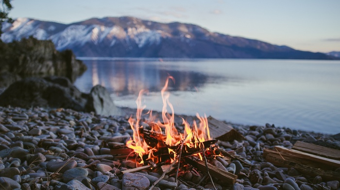 Campfire on a rocky shore with mountains and a lake