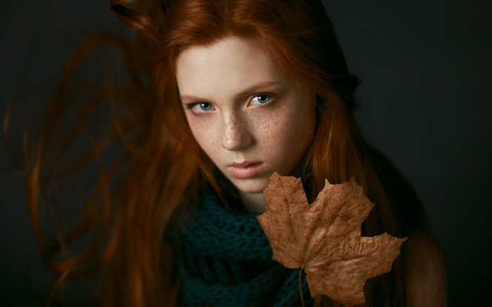 Redhead girl with freckles holding a leaf