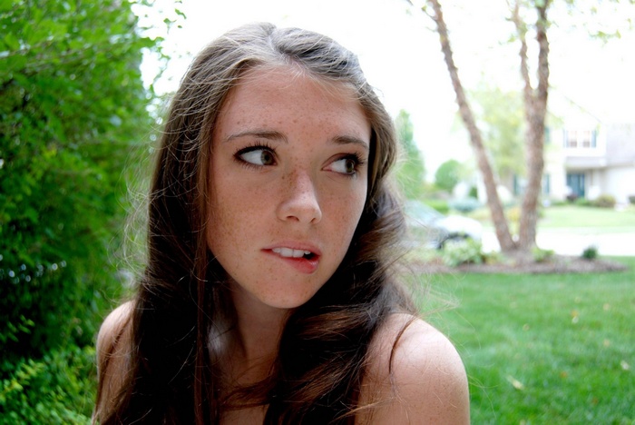 Woman with freckles biting her lip outdoors