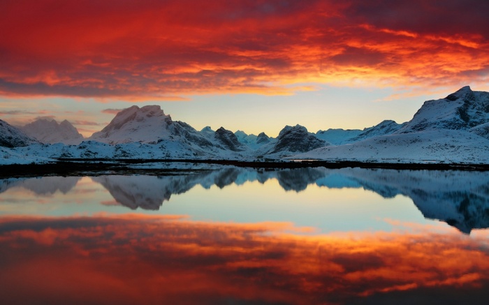 Snowy mountains reflected in a calm lake at sunset