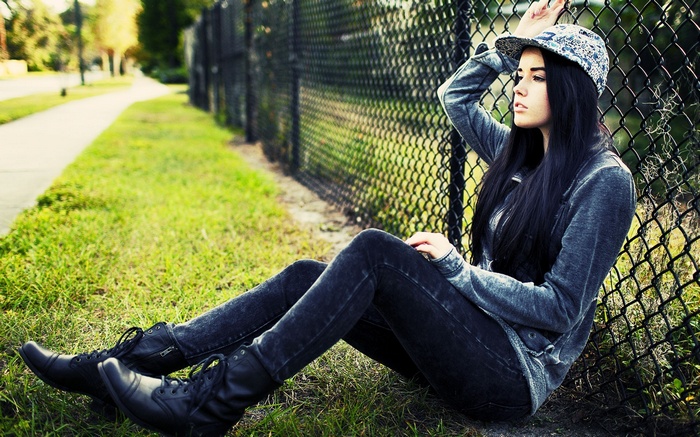 Woman with black hair sitting by a fence
