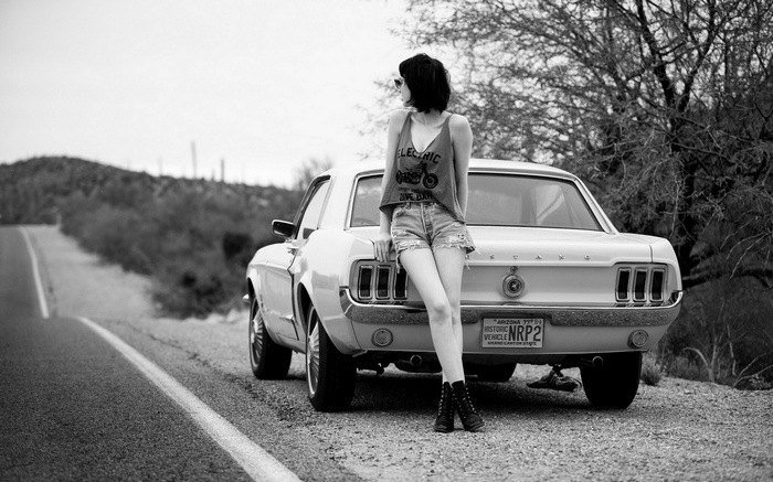 Woman leaning on a Ford Mustang on a desert road