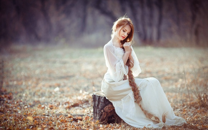 Redhead woman with long braids in a white dress outdoors