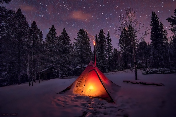 Tent in a snowy forest under a starry night sky