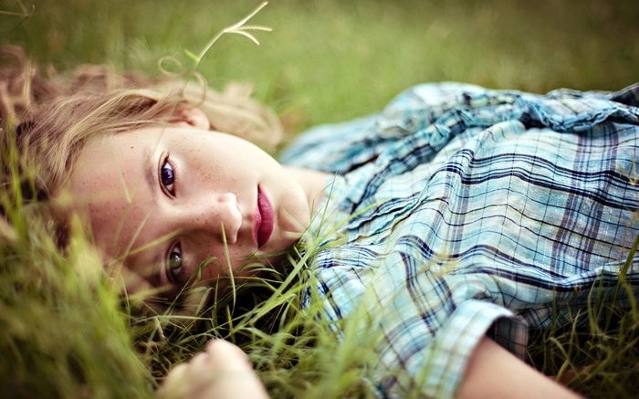 Girl lying in grass wearing a plaid shirt