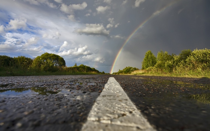 Wet road with a rainbow and storm clouds