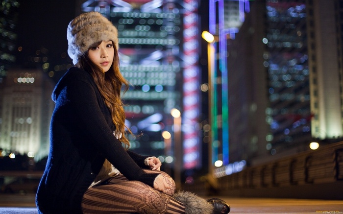 Asian woman in fur hat sitting in city at night