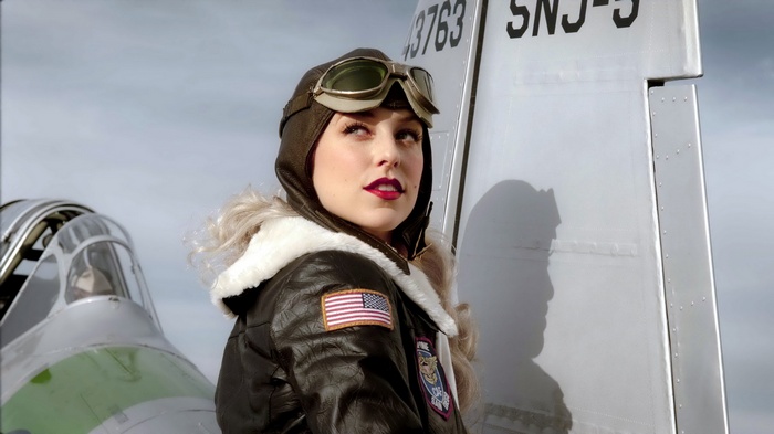 Woman pilot in vintage aviator gear posing by airplane