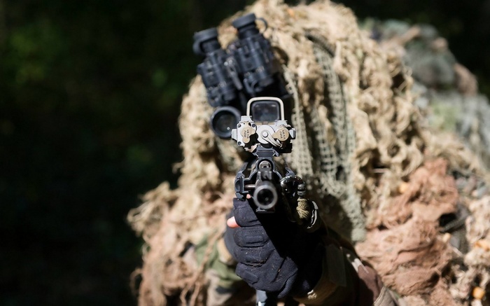 Sniper in camouflage aiming an AR-15 rifle