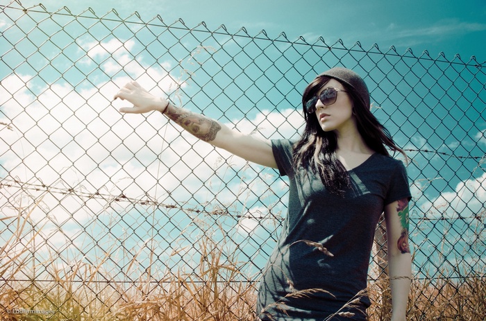 Woman with tattoos leaning on a fence