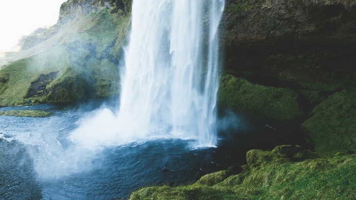 Waterfall cascading into a dark pool surrounded by mossy rocks