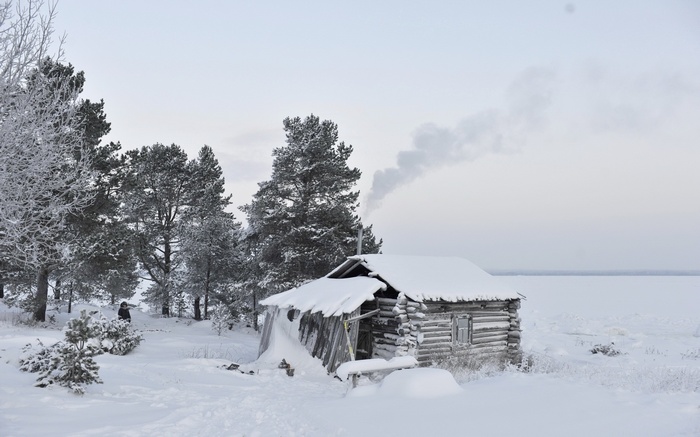 Winter landscape with a snow-covered log cabin and smoke from chimney