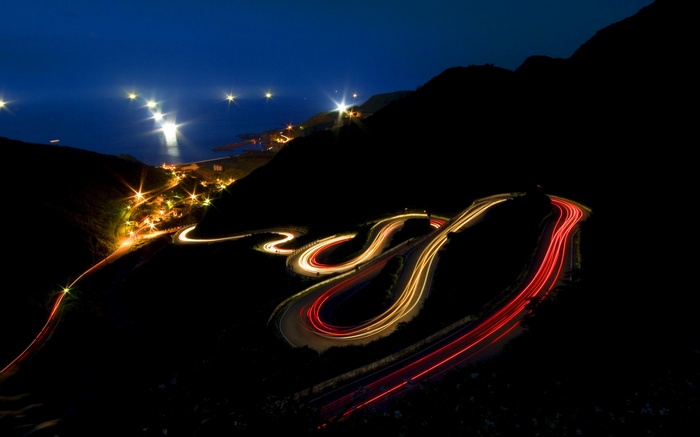 Nighttime mountain road with light trails and coastal town