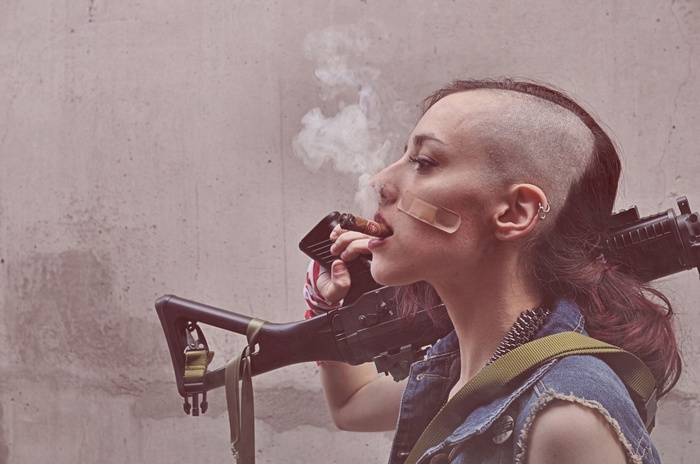 Woman with side shave smoking cigar and holding a machine gun
