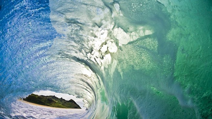 Inside a crashing ocean wave with a tropical island in the background