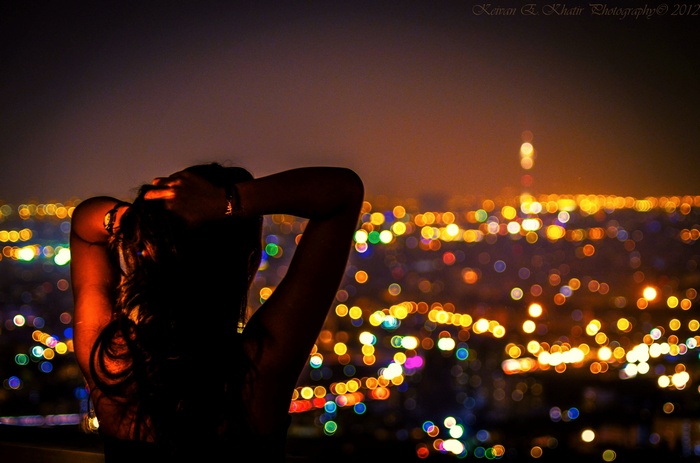 Woman with arms up looking at bokeh city lights at night