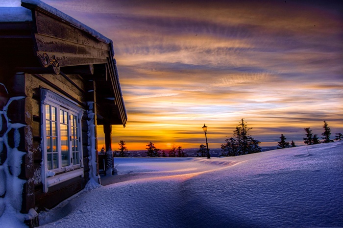 Log cabin in snowy landscape at sunset