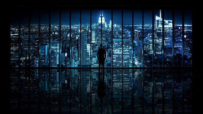 Silhouette of a man overlooking a nighttime cityscape through a window