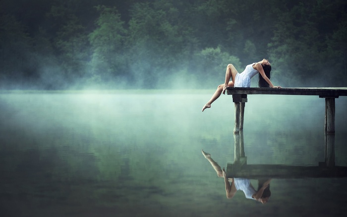 Woman in white dress on a wooden pier over a misty lake