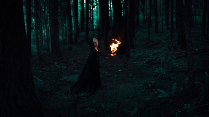 Woman in a black cloak holding fire in a dark forest