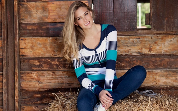 Bar Refaeli sitting on hay in front of a wooden wall