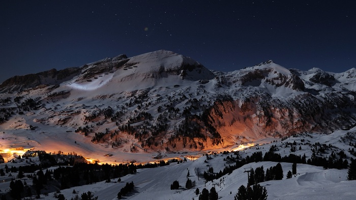 Snowy mountains at night with village lights and stars