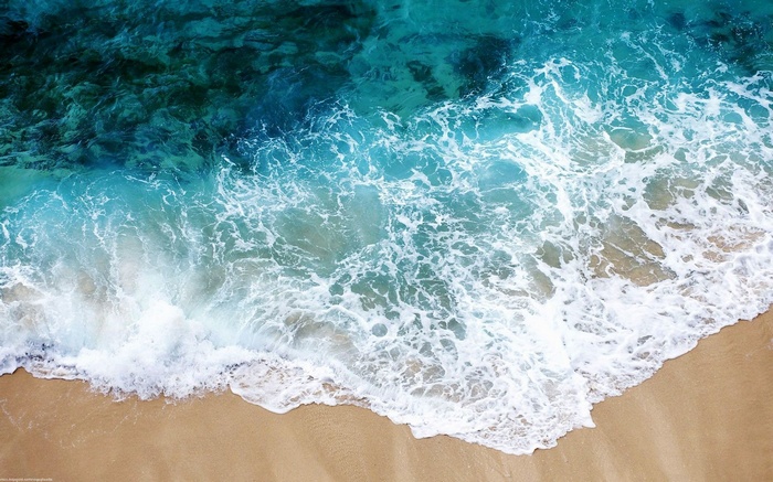 Aerial view of ocean waves crashing on a sandy beach