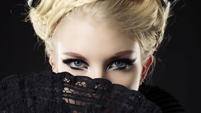 Woman with blue eyes and blonde hair holding a fan