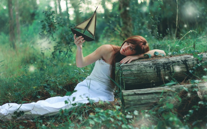 Redhead woman with a toy boat in a forest