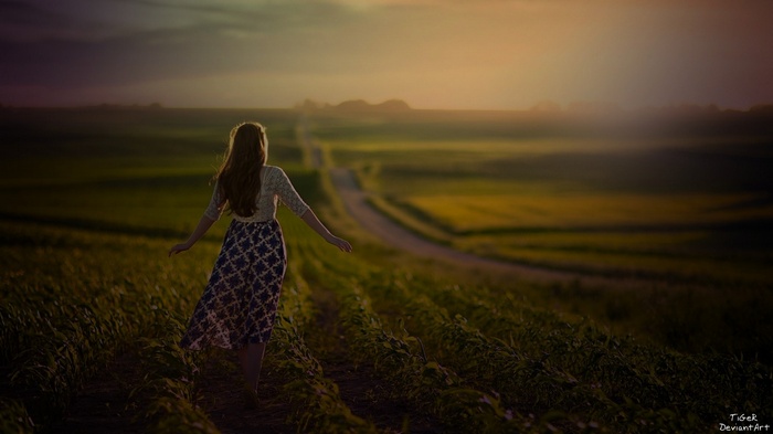 Girl walking on a path in a field at sunset