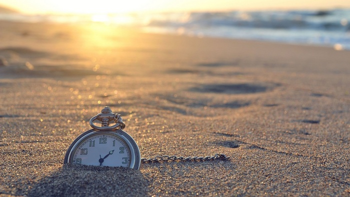 Pocket watch on a sandy beach at sunset